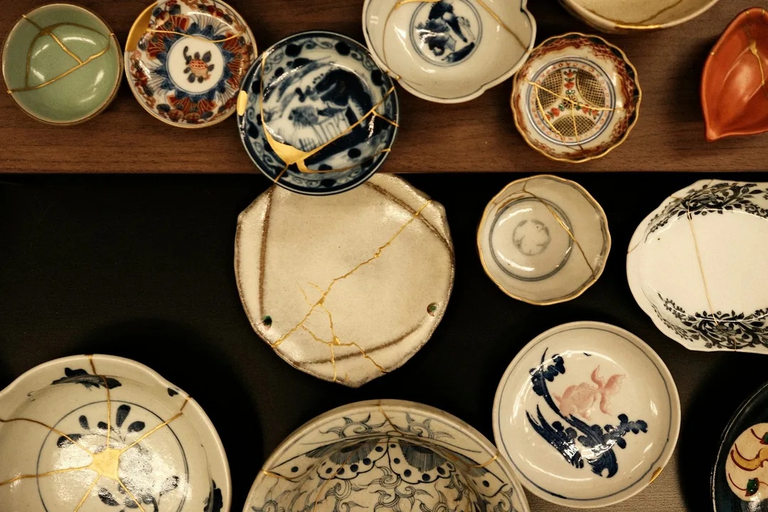 Keramické misky a talíře opravené kintsugi, se zlatými švy vedoucími přes lomy